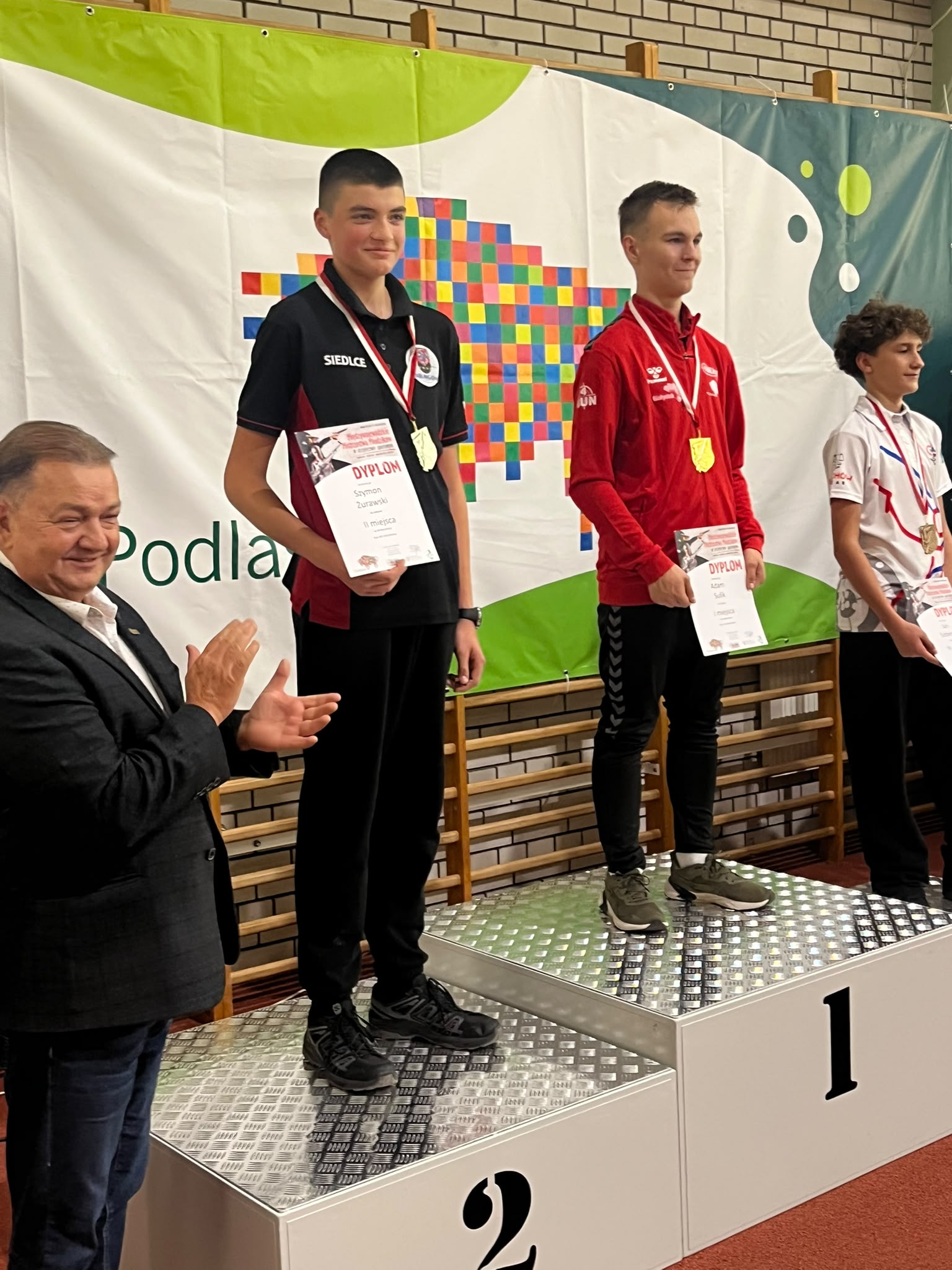 Szymon Żurawski na podium ze srebrnym medalem i dyplomem